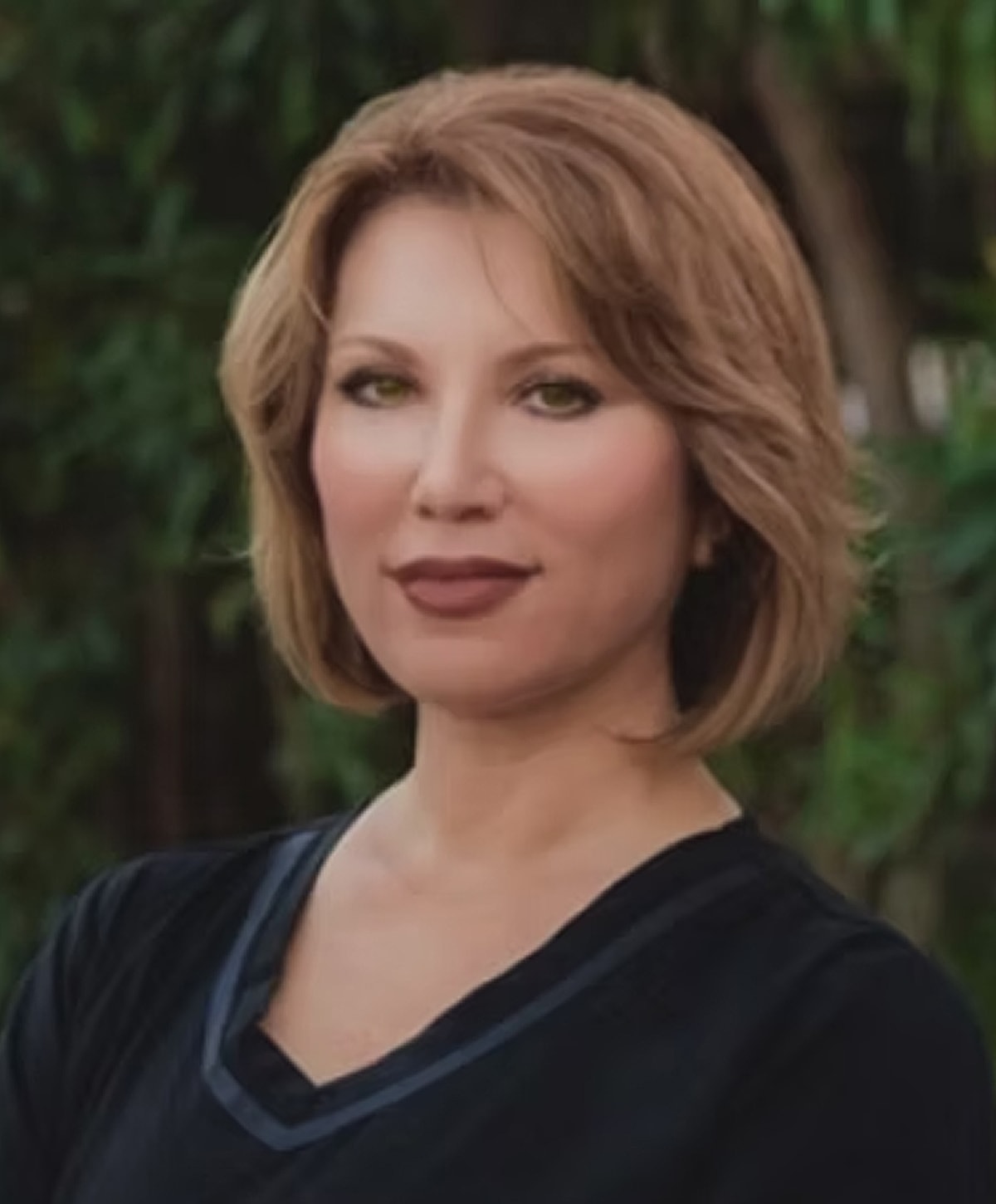 Smiling woman with shoulder-length brown hair outdoors.