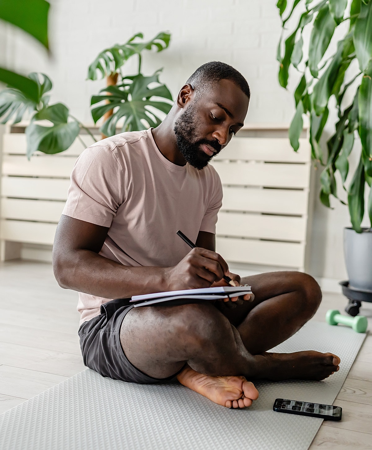 Man writing in notebook on exercise mat.