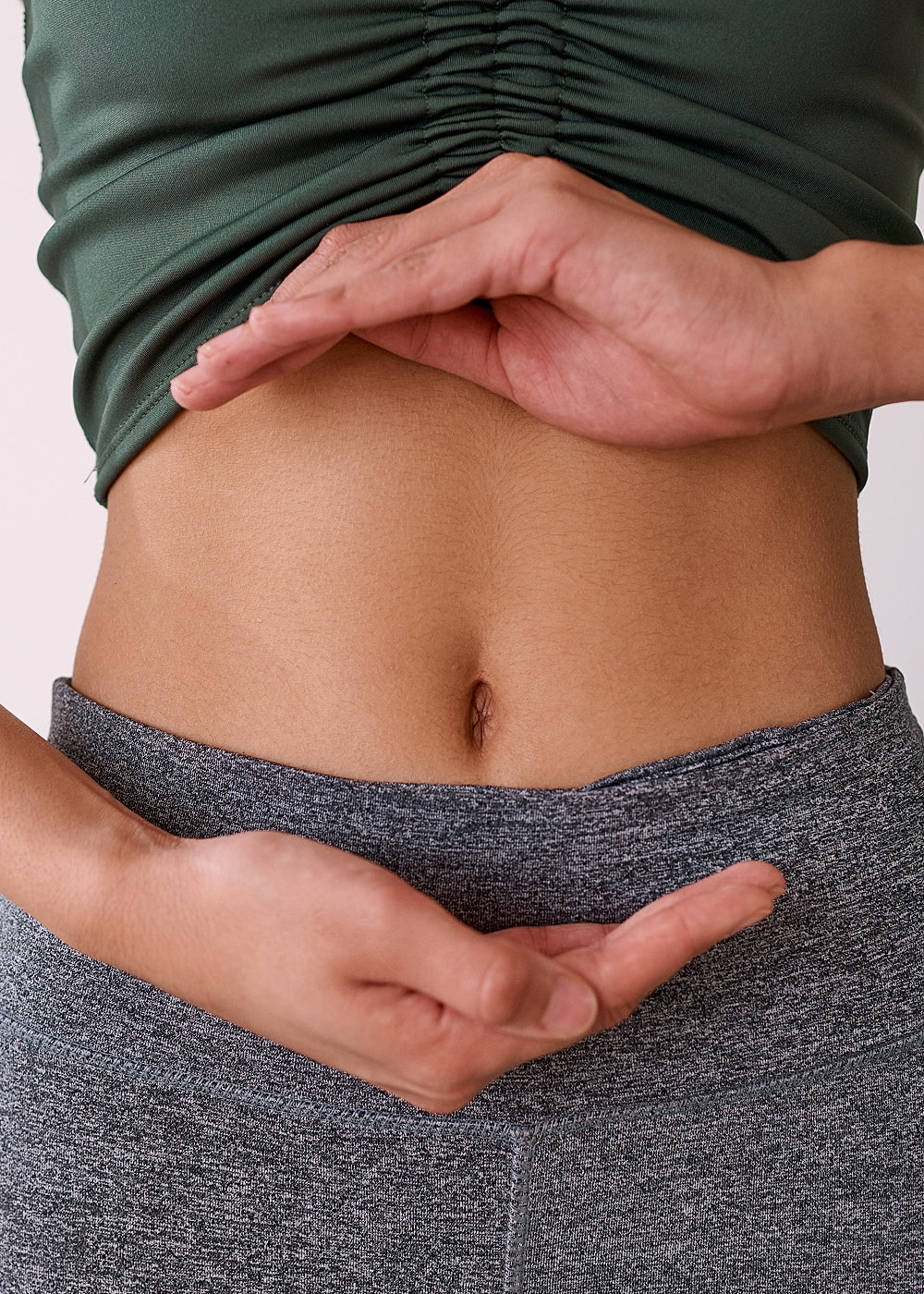 Hands framing a flat stomach in activewear.