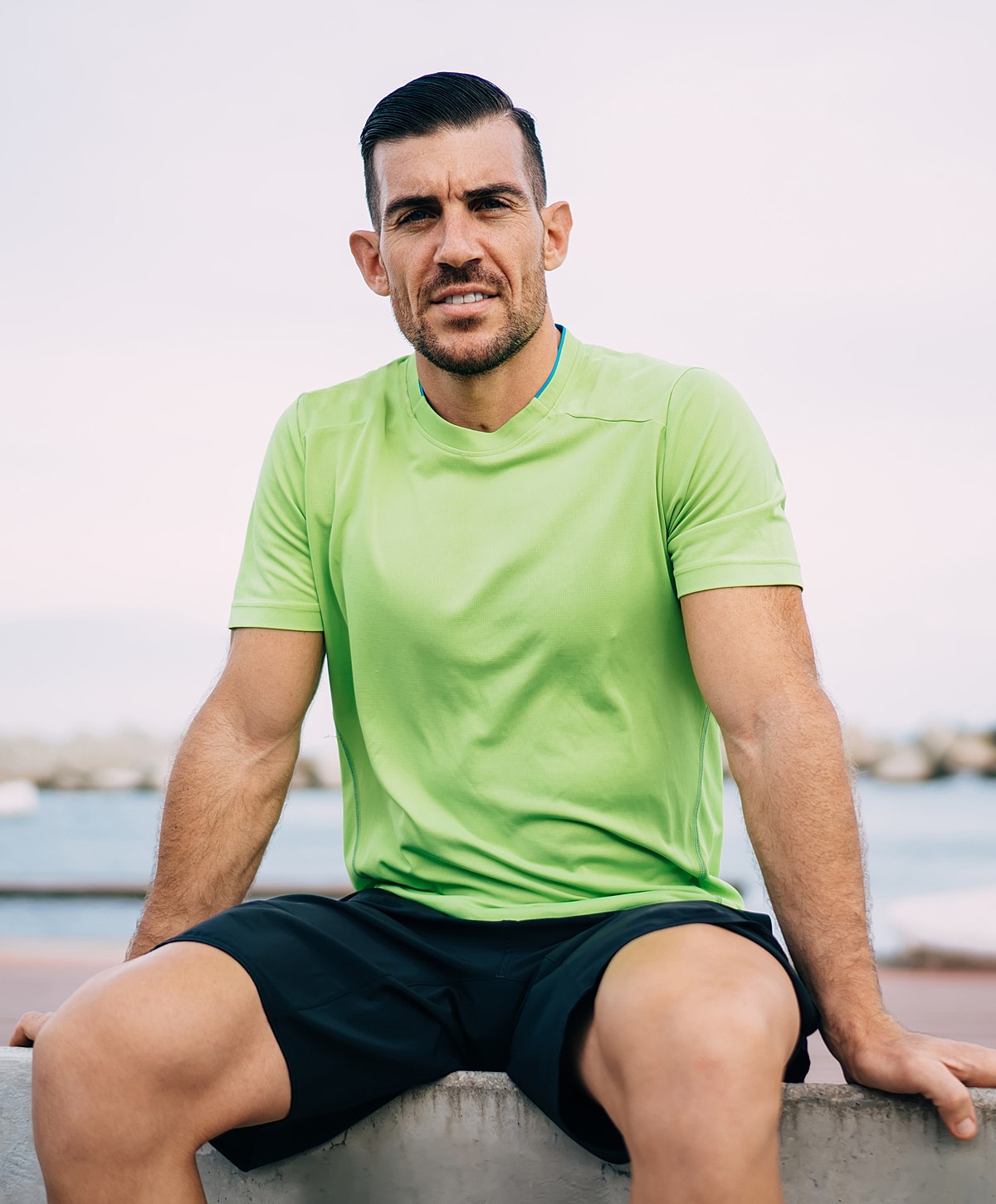 Man in green shirt sitting by the water.