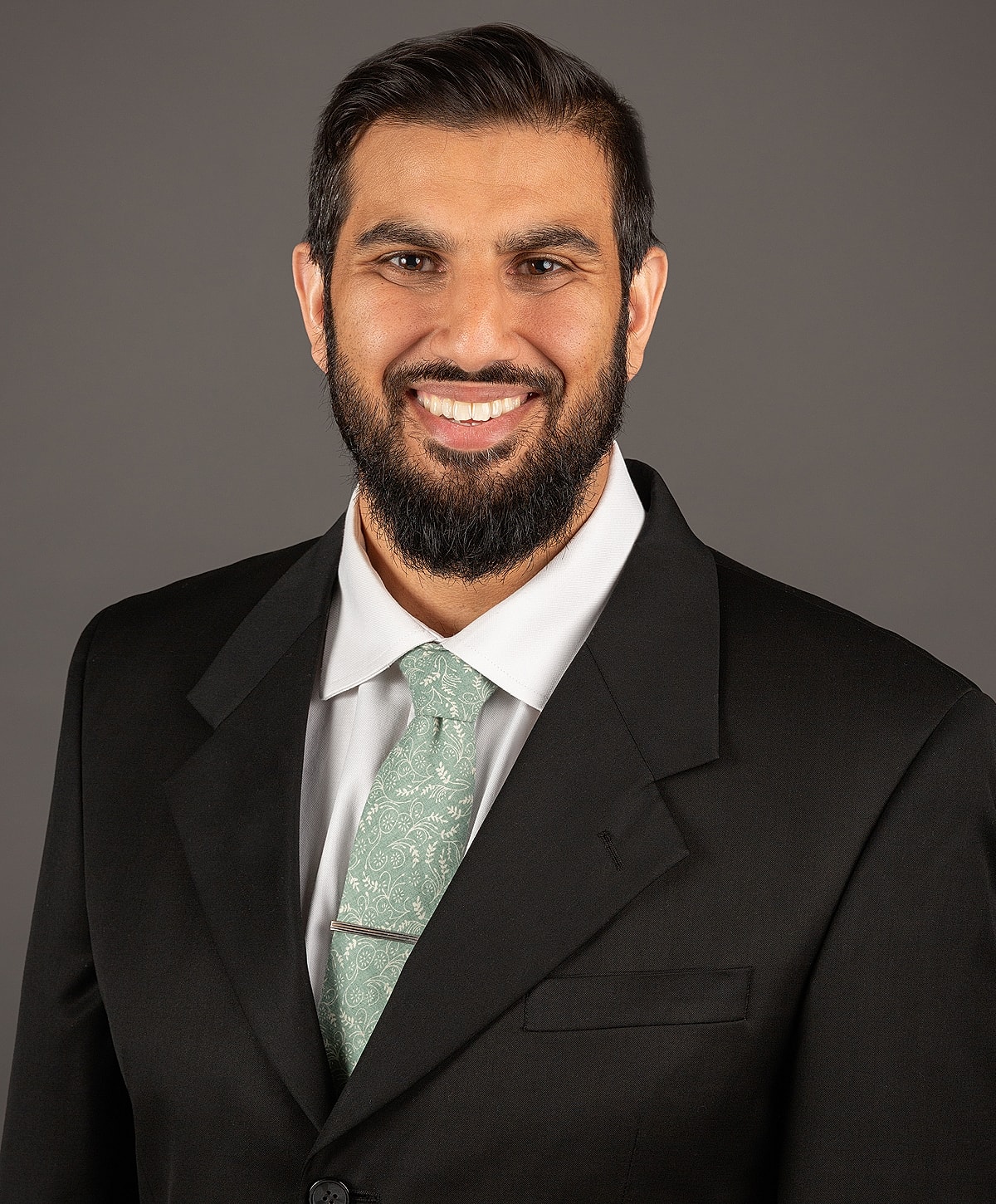 Smiling man in suit with tie against gray background.