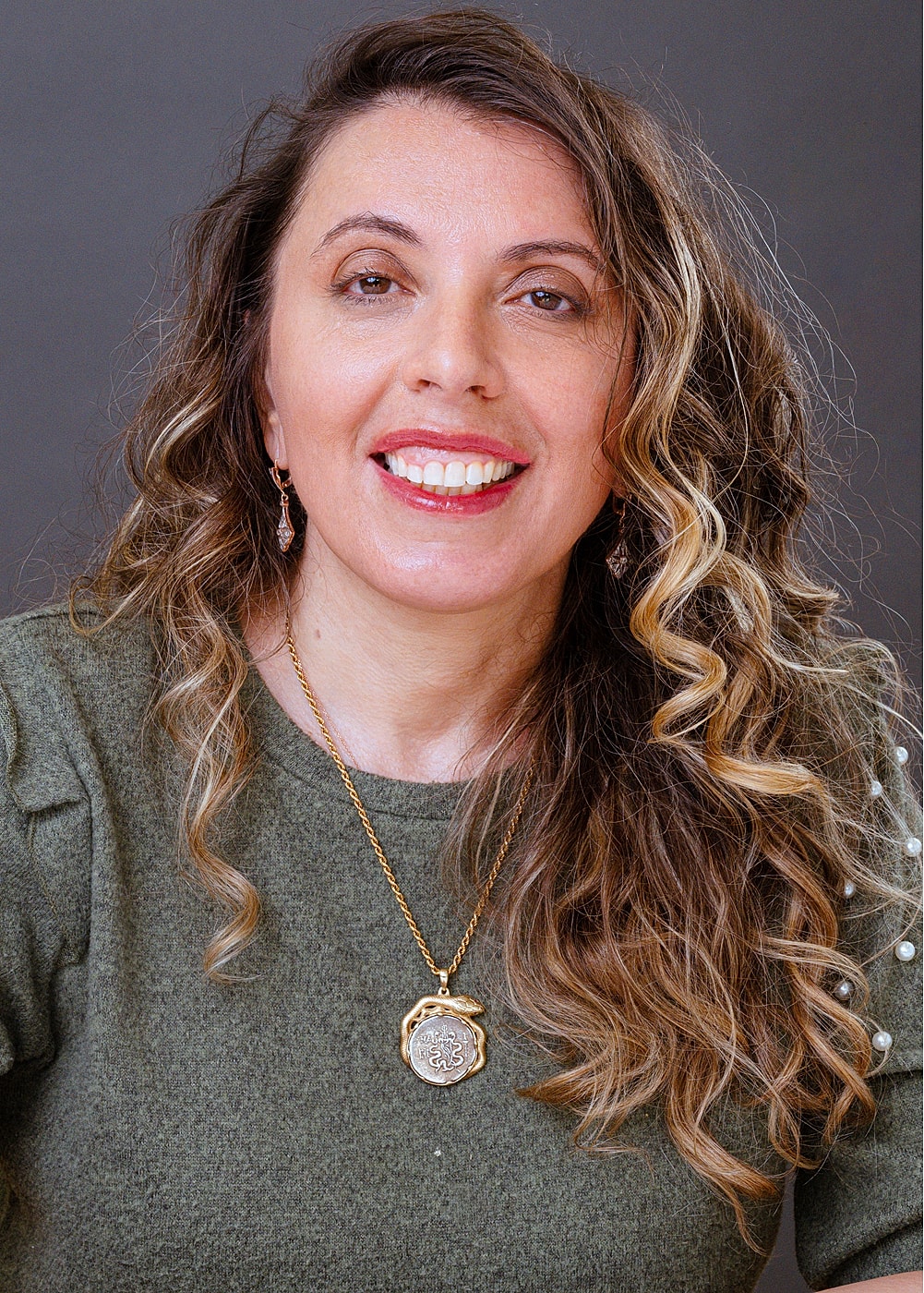 Smiling woman with curly hair and necklace.
