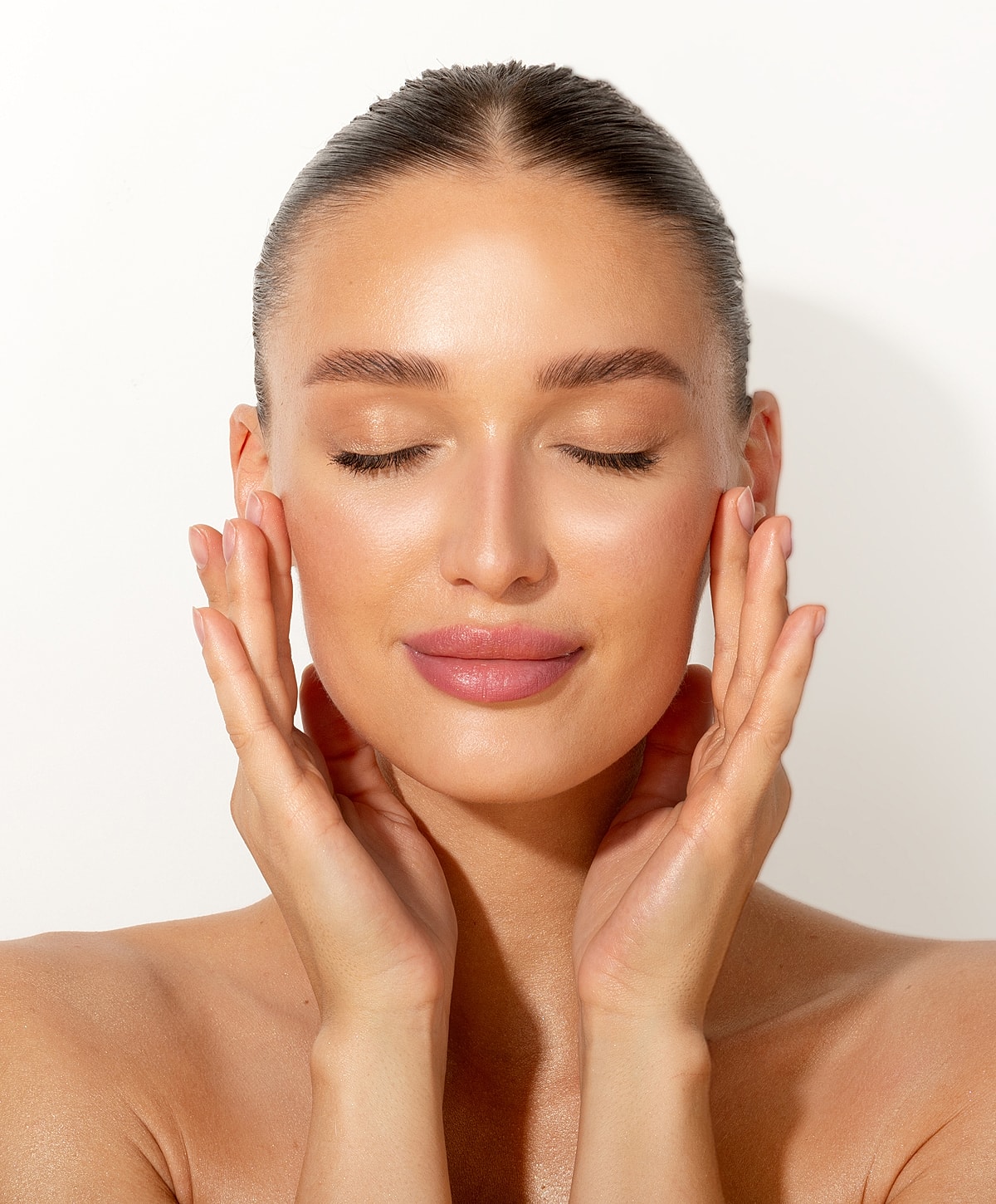 Woman with glowing skin, eyes closed, hands on face.