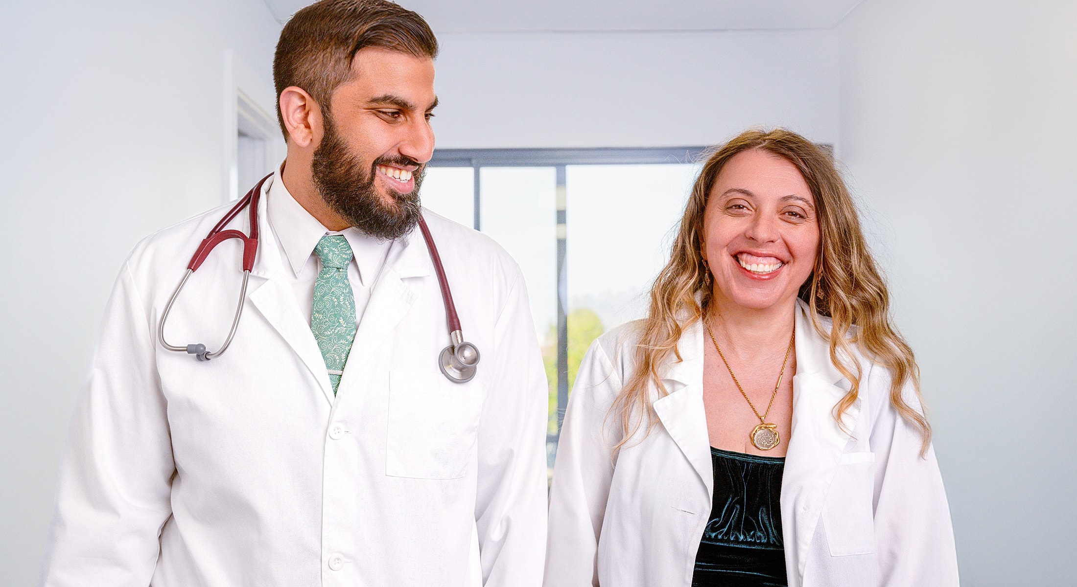 Two doctors smiling in a bright hallway.
